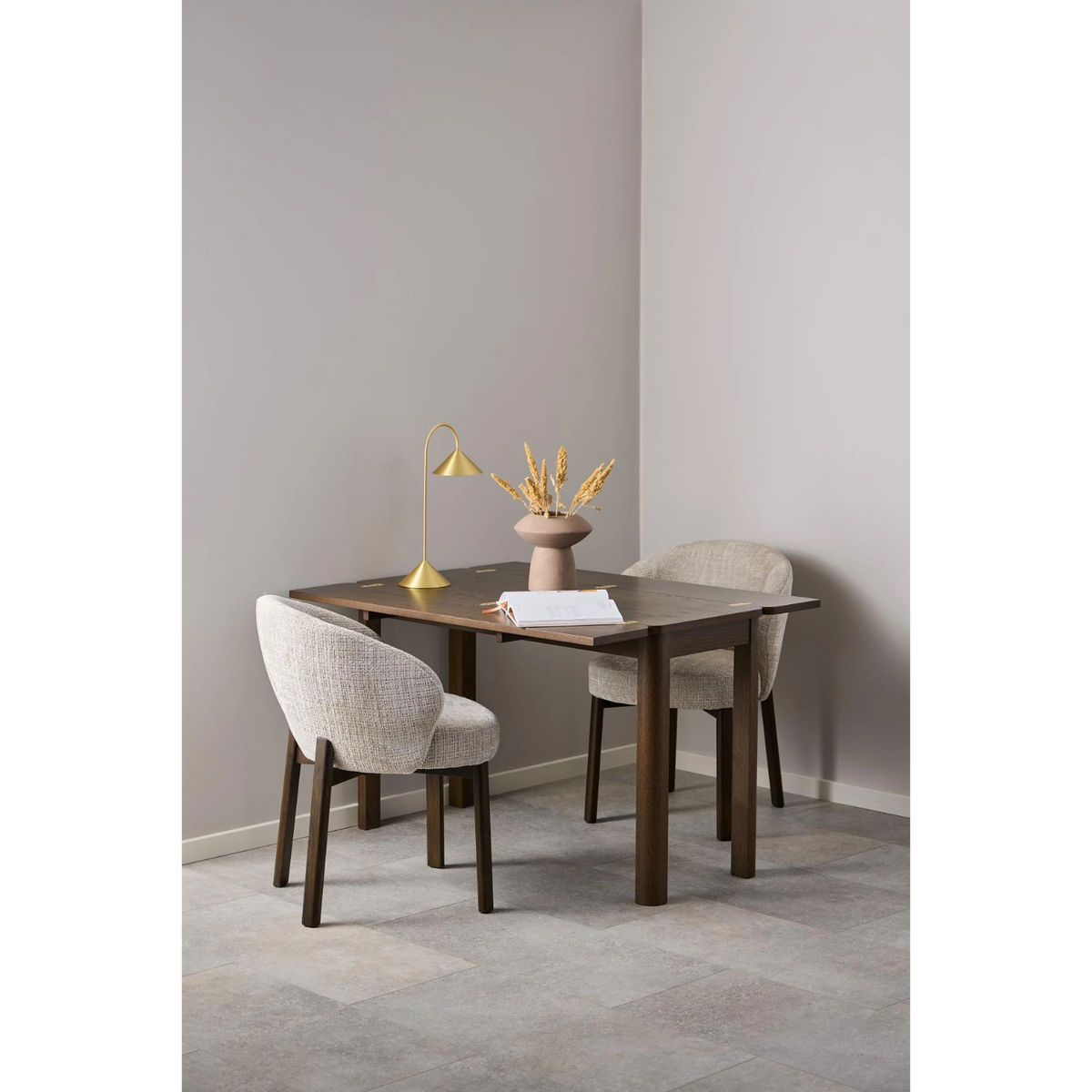 Moderner Esstisch aus dunklem Holz mit zwei beigen Stühlen und Dekoration in minimalistischem Design.