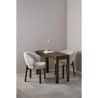 Moderner Esstisch mit zwei beigen Stühlen und goldener Stehleuchte in minimalistischem Design.