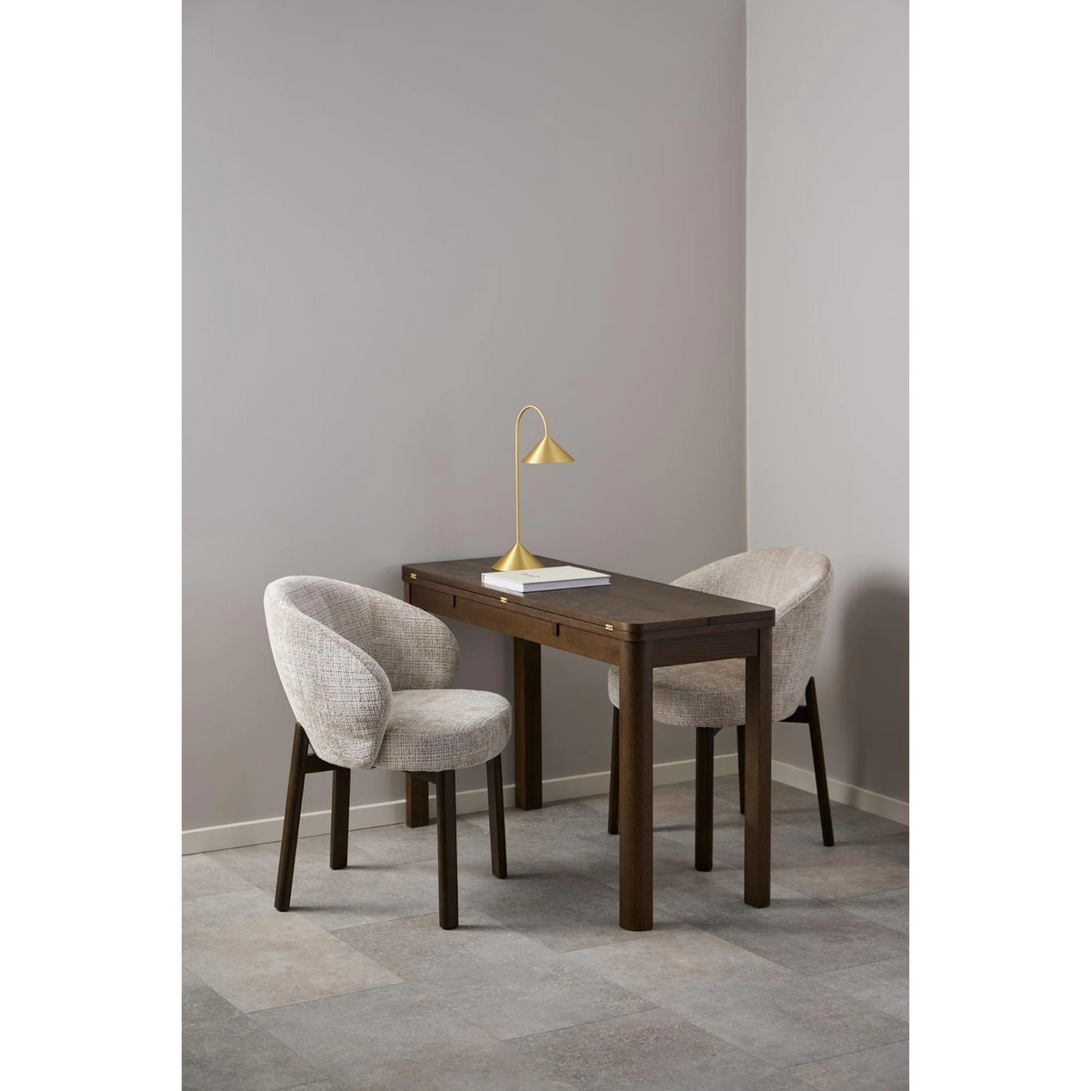 Moderner Esstisch mit zwei beigen Stühlen und goldener Stehleuchte in minimalistischem Design.