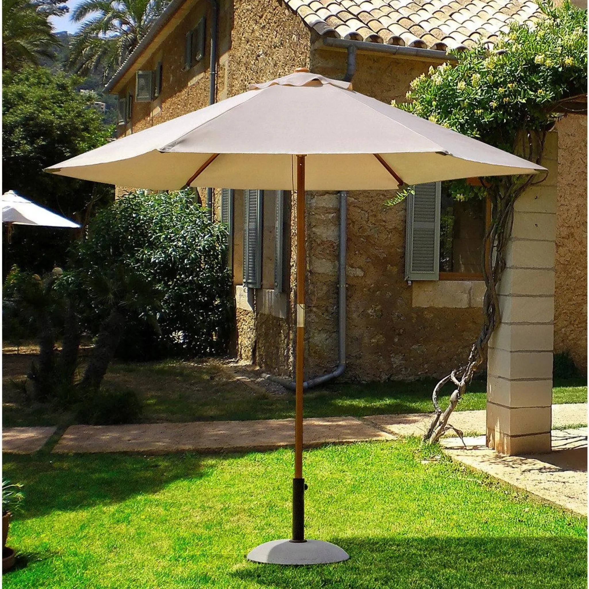 Beiger Sonnenschirm mit Holzmast und Granitständer im Garten vor mediterranem Haus