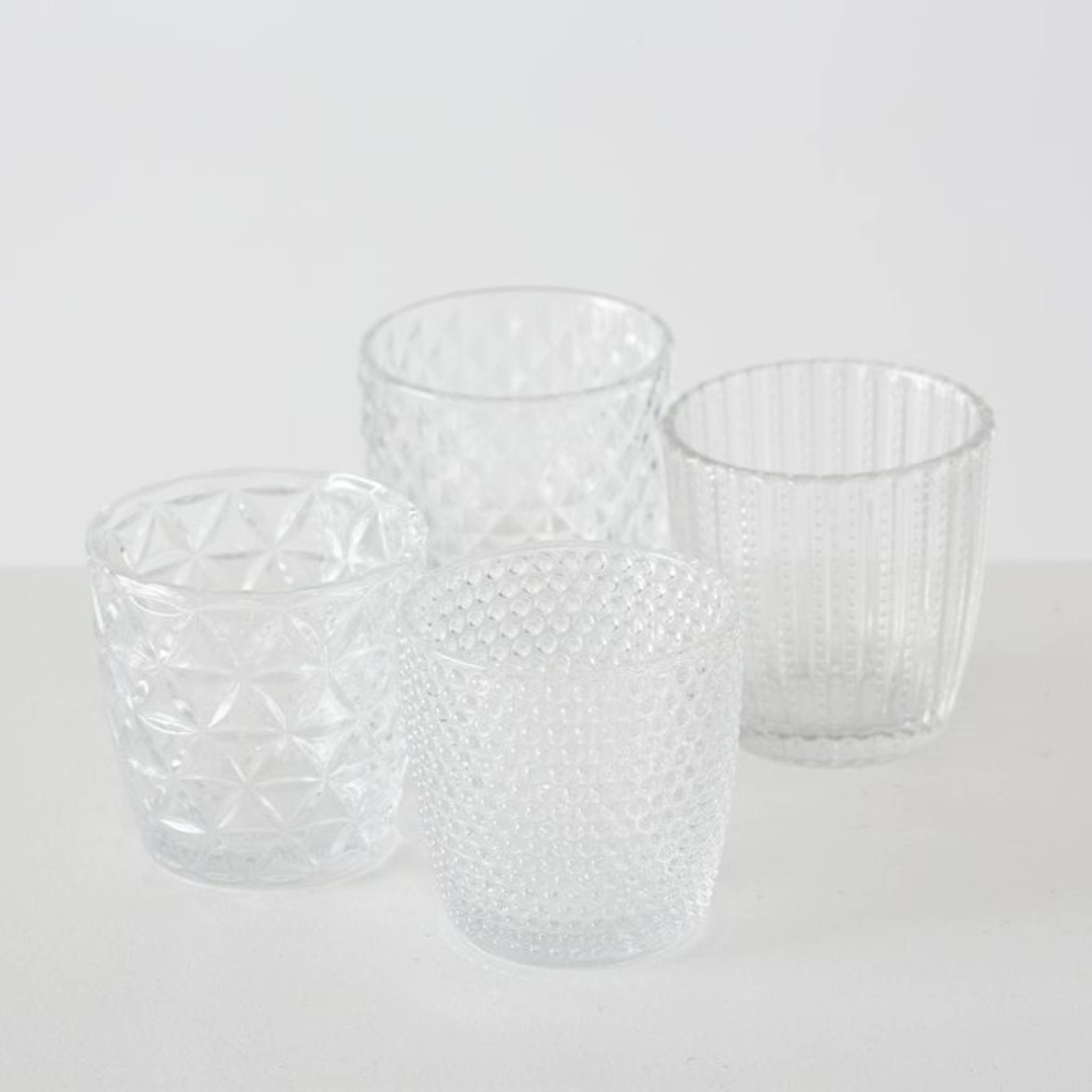 Vier verschiedene Klarglas-Teelichthalter mit unterschiedlichen Mustern und Texturen in modernem Design.