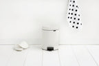 Brabantia Treteimer NewIcon 5L Weiss auf weissem Holzboden neben gepunkteter Serviette im minimalistischen Badezimmer