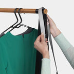 Kleiderständer Linn schwarz mit Holzstange, Person hängt Gürtel auf, grüne und graue Kleidung an schwarzen Bügeln