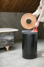 Brabantia Wäschekorb 60L in Schwarz mit Korkdeckel – Person legt Wäsche in modernen Badezimmer-Wäschesammler
