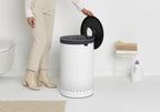 Brabantia Wäschekorb 60L Weiss mit schwarzem Deckel, Frau öffnet Korb im modernen Badezimmer