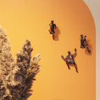 Drei KARE Climber Wandfiguren in Bronze auf orangefarbener Wand mit dekorativem Trockenblumen-Arrangement