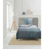 Kremer Bettwäsche-Set in Ternetblau auf modernem Einzelbett mit grauem Kopfteil in hellem Schlafzimmer