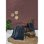 Jeans-blaue Fleecedecke auf gemustertem Sessel mit Jute-Teppich und Zimmerpflanze vor dunkelroter Wand