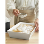 Weisse quadratische Gratinform mit frischen Hefebrötchen, bestäubt mit Puderzucker durch ein Sieb