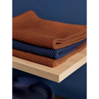 Gefaltete Baumwolltücher in Rostbraun und Dunkelblau auf Holzregal – ASA Baumwolltuch DeepBlue 30x30