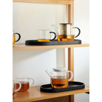 Ovales schwarzes Tablett auf Holzregal mit Glasteekanne und Teetassen mit Tee