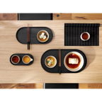 Schwarzes ovales ASA-Tablett mit japanischen Speisen, Stäbchen und Schalen auf hellem Holztisch