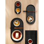 Schwarzes ovales ASA-Tablett mit japanischen Speisen, Stäbchen und Schalen auf hellem Holztisch