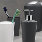 Badezimmer-Set in Grau: Schwingdeckeleimer, Seifenspender, Zahnbürstenhalter und weiße Tasse mit Zahnbürsten