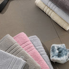 Gefaltete Handtücher in Grau, Rosa und Beige auf Fliesenboden mit Kristall-Dekoration