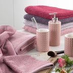 Stapel gefalteter Handtücher in Pink, Lila und Rot mit Seifenspender, Zahnbürstenhalter und Kosmetikpinsel