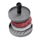 Hamburger-Presse aus Aluminium mit schwarzem Griff und rohem Hackfleisch-Patty auf Antihaftpapier