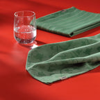 Kela Geschirrtuch Cora in Grün mit Blumenmuster auf rotem Untergrund, daneben ein Wasserglas