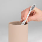 Hand legt weiße Zahnbürste in beigen Keramikbecher Kela Sana – moderner Badezimmer-Zahnbürstenhalter