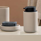 Kela Seifenspender Sana Beige mit schwarzem Pumpkopf, Seifenschale und Becher auf weißer Ablage
