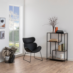 Actona Seaford Regal mit 4 Ablagen in Schwarz, dekoriert mit Büchern und Vase, neben schwarzem Sessel im modernen Wohnzimmer