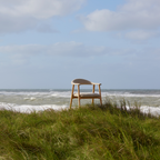 Actona Addi Armlehnstuhl Beige auf Stranddüne mit Meeresblick – moderner Holzstuhl mit gepolstertem Sitz