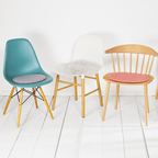 Drei Stühle mit runden Sitzkissen: Eames-Stuhl türkis, weißer Schalenstuhl mit Lammfell-Kissen, Holzstuhl rosa