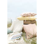 Pastellfarbene Kissenhüllen in Rosa und Gelb auf Holzkiste am Strand mit weißer Strickdecke und Magazin