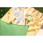 Grünes Outdoor-Kissen auf Holzliege mit gelbem Überwurf und Gläsern mit Zitronenwasser im Garten