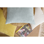 Mintgrünes Cord-Kissen auf Holzsofa mit gelbem Kissen, cremefarbenem Zierkissen und Magazin auf Teppich