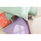 Dekorative Kissen in Mintgrün, Lila und Beige auf einem Sofa mit einem Buch im Hintergrund
