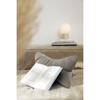 Graues Cord-Lesekissen mit aufgeschlagenem Buch auf beigem Sofa, dekorative Kugellampe im Hintergrund