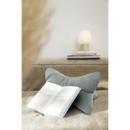 Graues Cord-Buchkissen als Buchständer mit aufgeschlagenem Buch auf beigem Sofa, Tischlampe im Hintergrund