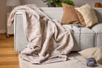 Biederlack Kuscheldecke Feel Leo in Beige auf hellem Sofa mit Dekokissen und Wollknäuel