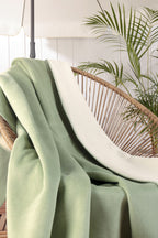 Biederlack Kuscheldecke Doubleface in Mint auf Rattan-Sessel mit Zimmerpflanze im Hintergrund