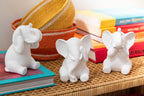 Drei weisse Elefanten-Figuren auf Rattan-Tisch mit bunten Büchern und Korb-Dekoration
