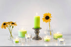 Grüne Duftkerzen und Teelichter mit Sonnenblumen auf weißem Tisch – stimmungsvolles Kerzen-Arrangement