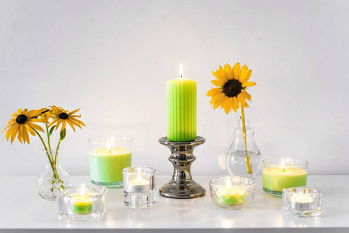 Grüne Duftkerzen und Teelichter mit Sonnenblumen auf weißem Tisch – stimmungsvolles Kerzen-Arrangement