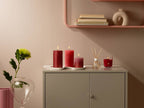 Bolsius Geschenkset Fruit Splash Granatapfel: 3 rote Duftkerzen und Reed Diffuser auf grauem Sideboard