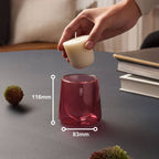 Bolsius Duftkerzen-Starterkit: Hand platziert cremefarbenen Nachfüller in rosa Glas-Halter (116x83mm) auf grauem Tisch