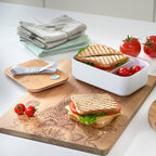 Zeller Schneidebrett aus Holz mit Mandala-Gravur, belegt mit gegrilltem Sandwich, Tomaten und Lunchbox