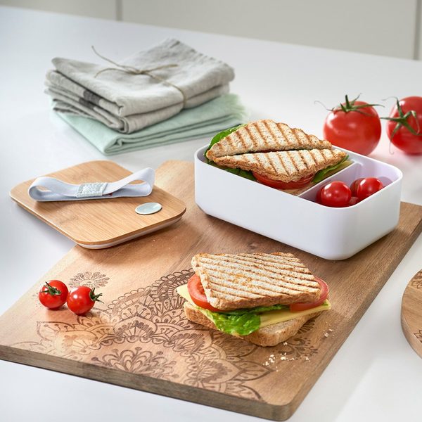 Zeller Schneidebrett aus Holz mit Mandala-Gravur, belegt mit gegrilltem Sandwich, Tomaten und Lunchbox