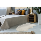 Lalee Kunstfell Teppich Cosy in Creme vor modernem Bett mit Holz-Nachttisch und Zierpflanzen