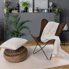 Moderne Wohnzimmer-Einrichtung mit braunem Butterfly-Sessel, weißer Kuscheldecke und Pflanzen