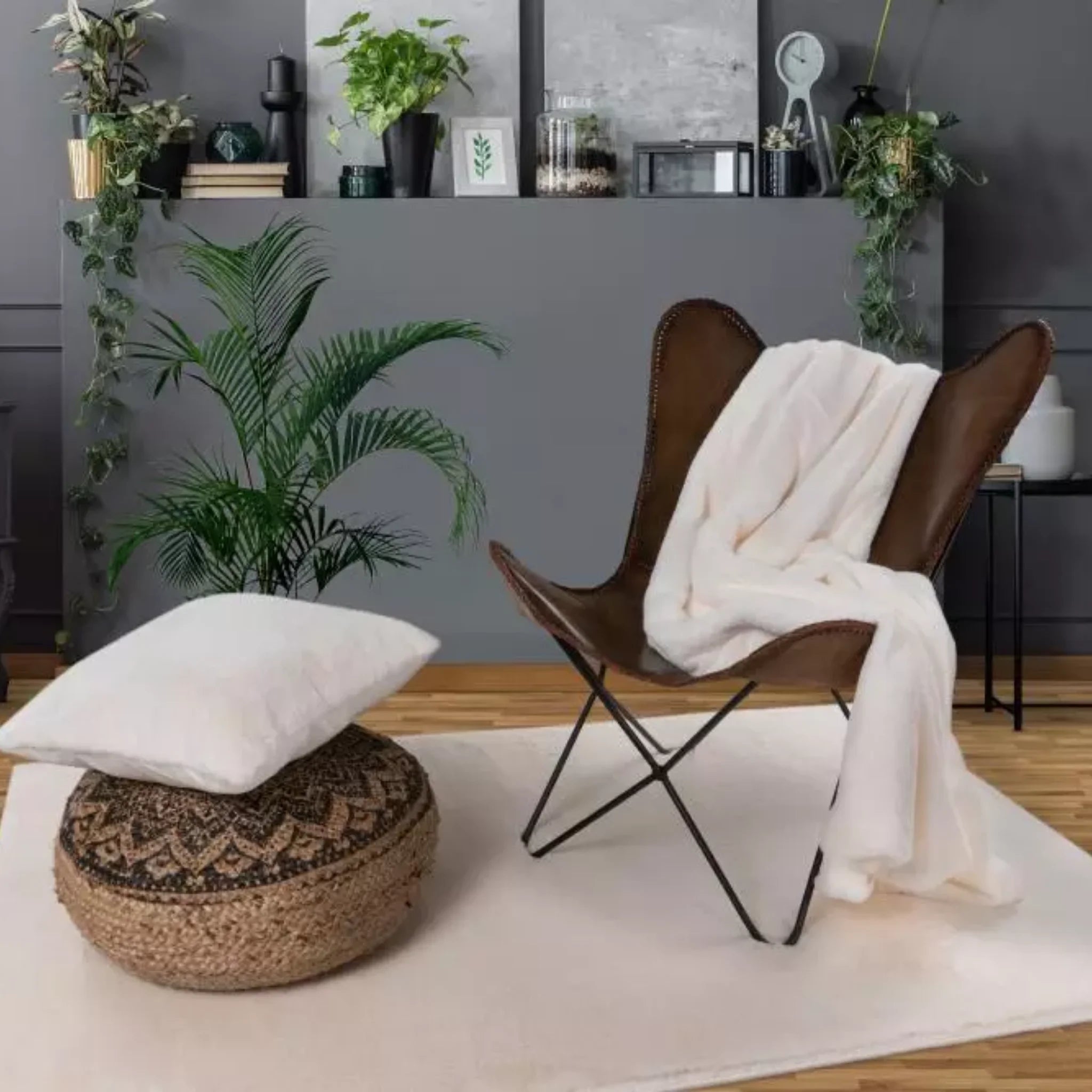Moderne Wohnzimmer-Einrichtung mit braunem Butterfly-Sessel, weißer Kuscheldecke und Pflanzen