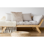 Gemütliches Boho-Wohnzimmer mit beigen Kissen auf Holzsofa, Makramee-Decke und geflochtenem Pouf