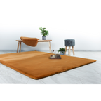 Lalee Heaven Teppich in warmem Cognac-Braun, flauschig weich, auf hellem Parkettboden mit Holzbank und Zimmerpflanzen