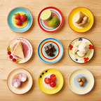 Neun bunte Teller mit Lebensmitteln: Erdbeeren, Limette, Ingwer, Käse, Schokolade, Knoblauch, Zwiebel, Tomaten und Nüsse.