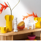 Weiße Elefantenpyramide Deko mit gelben Vasen und orangen Blüten auf Holzkommode