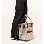# Alt-Text für das Bild:

Rosa glänzende Beutler Hulken Medium Handtasche mit Rollen, getragen von Frau in schwarzem Outfit
